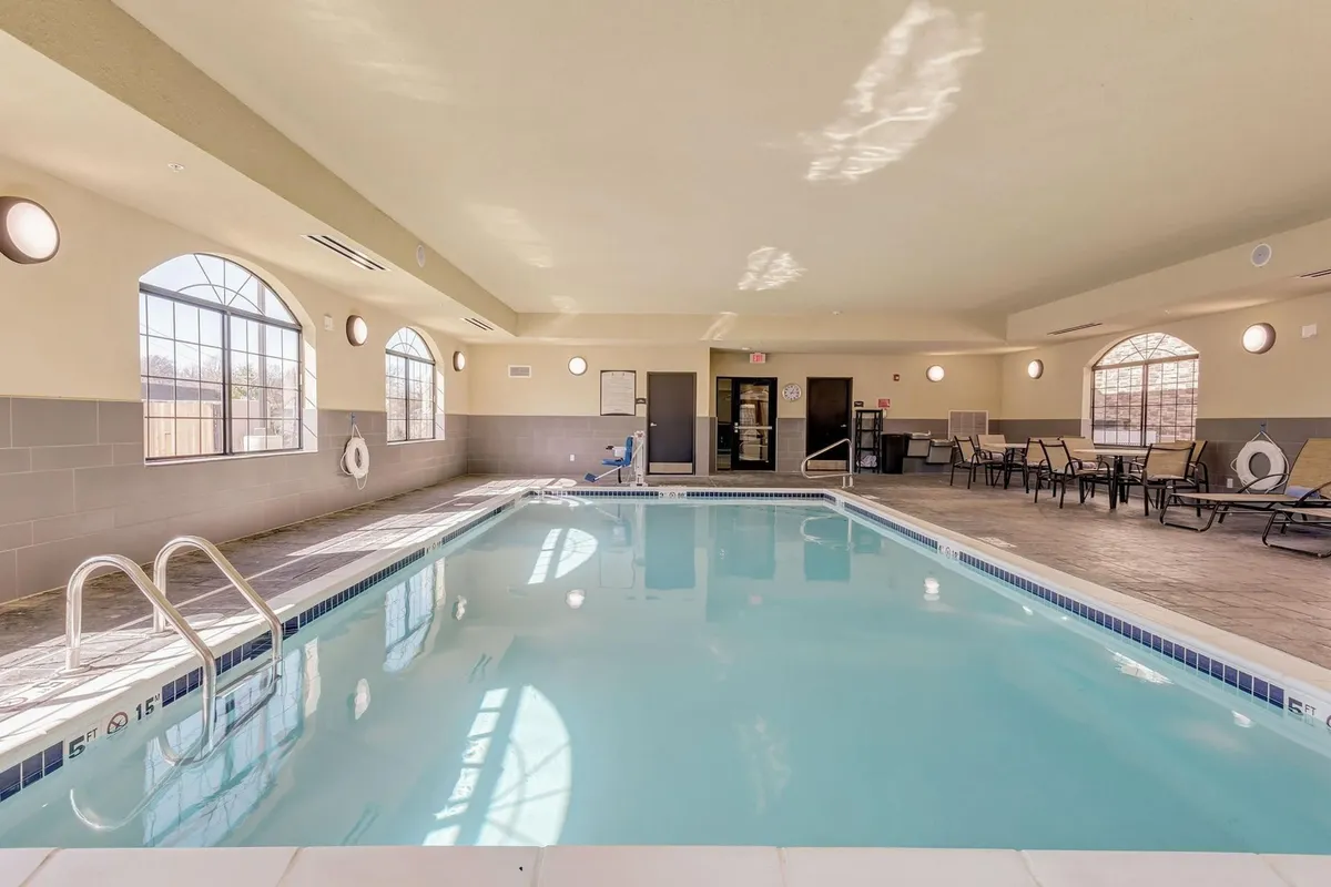 The image highlights a serene indoor swimming pool area, filled with natural light from large windows. Lounge chairs line the poolside, inviting guests to relax after a busy day. The atmosphere is peaceful, with subtle cues of families enjoying a splash, quiet reading by the water, and the potential for a soothing evening swim. The setting suggests both a restorative and social space within the property.