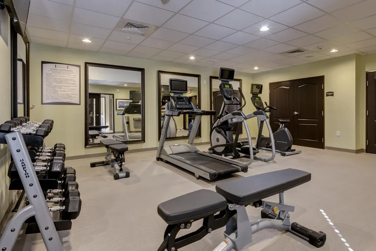 A fully equipped fitness center featuring a treadmill, elliptical machine, dumbbell rack, and weight bench. The layout is spacious, inviting guests to engage in both cardio and strength training activities in a modern, energetic setting.