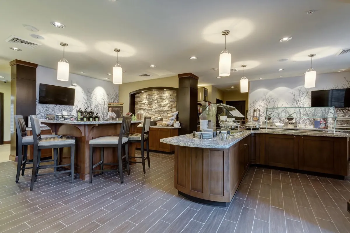 This image showcases a stylish interior dining area featuring a wooden bar with high chairs, a stone feature wall, and a visible buffet area with glass display. The setup conveys a relaxed, social atmosphere ideal for enjoying self-serve meals, breakfast, or casual dining with others.