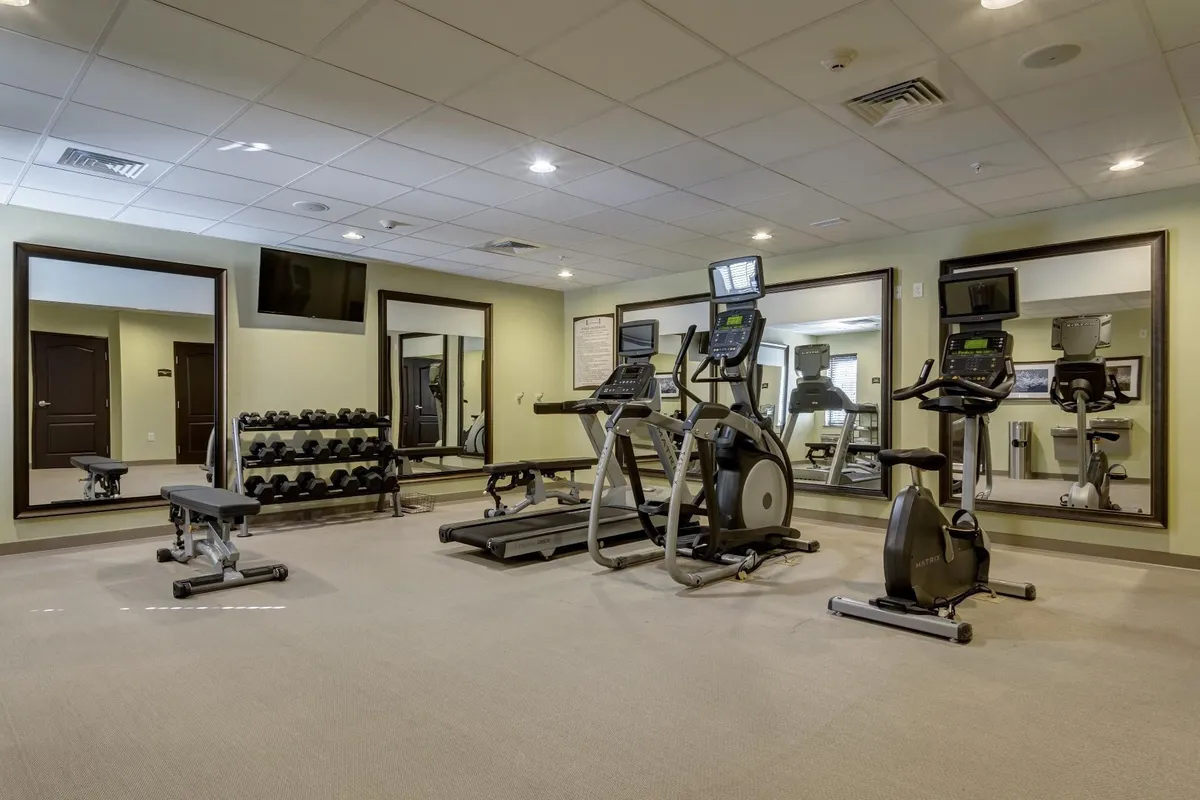 This interior image features a well-equipped fitness center with a variety of exercise machines, free weights, and mirrors, fostering an energetic and focused environment. The setup invites guests to maintain their workout routines, whether solo or as part of a group.