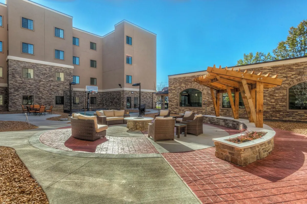 This exterior image captures a welcoming outdoor seating area with a fire pit under a pergola, inviting guests to gather for relaxed evening meals or social events. The setting is perfect for barbecuing and unwinding after a busy day.