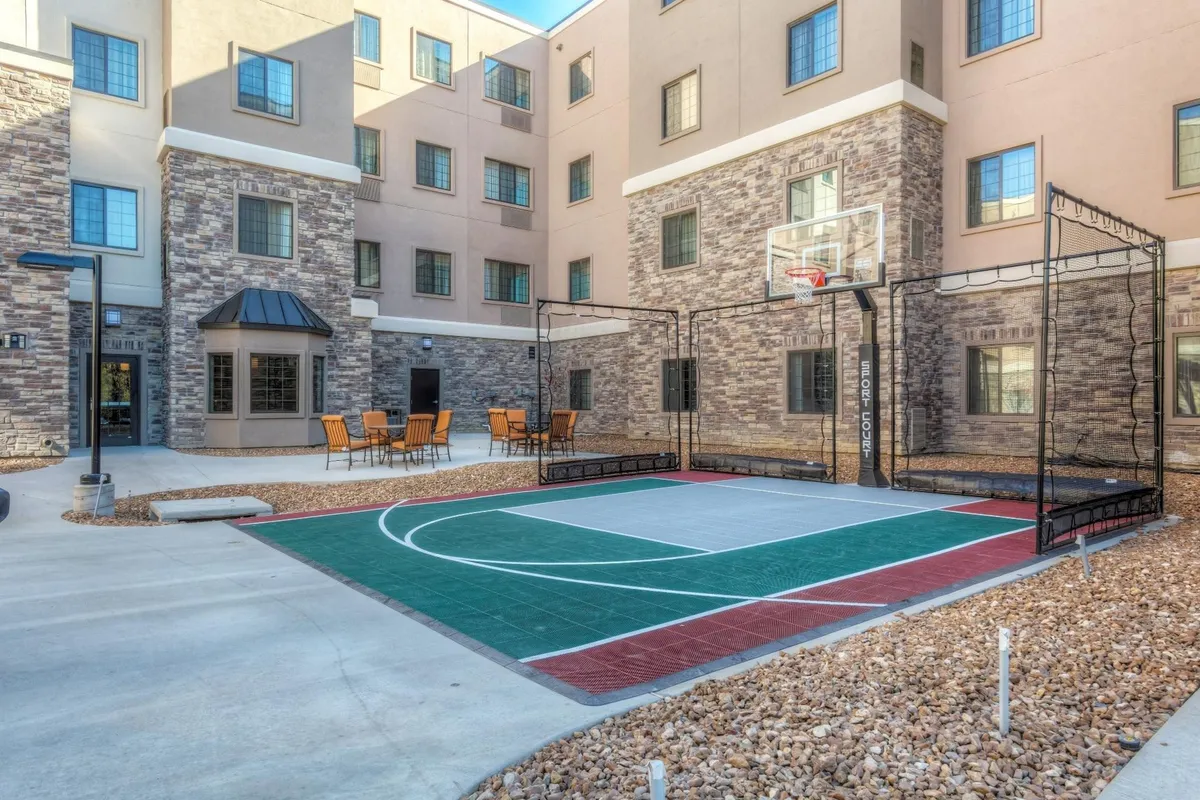This image captures an energetic exterior scene featuring a basketball court, seating area, and surrounding hotel architecture. Families and guests can be seen enjoying playful activities and social gatherings, highlighting options for outdoor recreation on the property.
