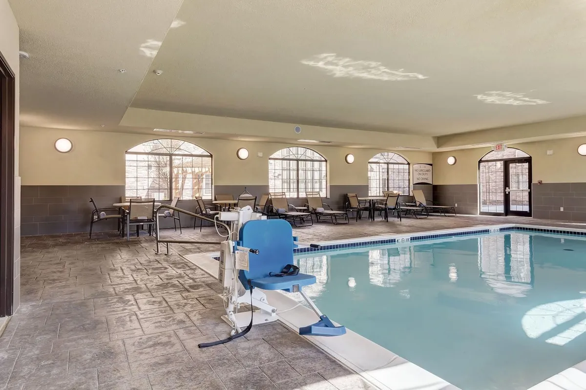 This image showcases a bright, welcoming indoor swimming pool area with large arched windows, comfortable poolside seating, and an accessible swimming lift. The scene conveys a sense of relaxation and inclusivity, highlighting both leisurely swims and opportunities for guests to socialize or unwind by the water.