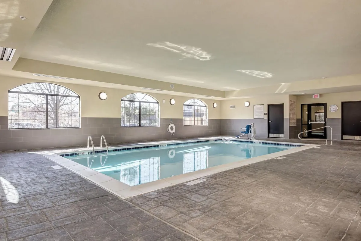 An inviting indoor swimming pool area with large windows, poolside seating, and visible safety equipment. The tranquil space is ideal for relaxing swims or quiet moments after a busy day.