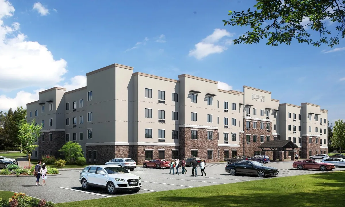 This exterior image showcases the welcoming facade of Staybridge Suites St Louis - Westport. The scene features the building's entrance awning, landscaped areas, parking lot, and guests walking by, creating a vibrant and inviting atmosphere for arriving families.