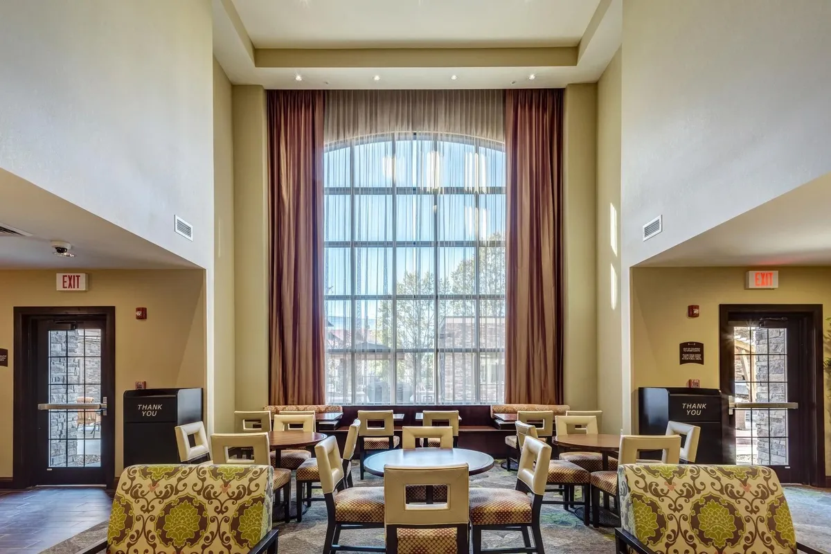 A sunlit seating area with a large arched window, stylish decorative chairs, and a welcoming vibe. The space feels airy and relaxing, ideal for unwinding, reading, or socializing. It's designed to evoke a sense of home, with unique decor adding personality to the suite.